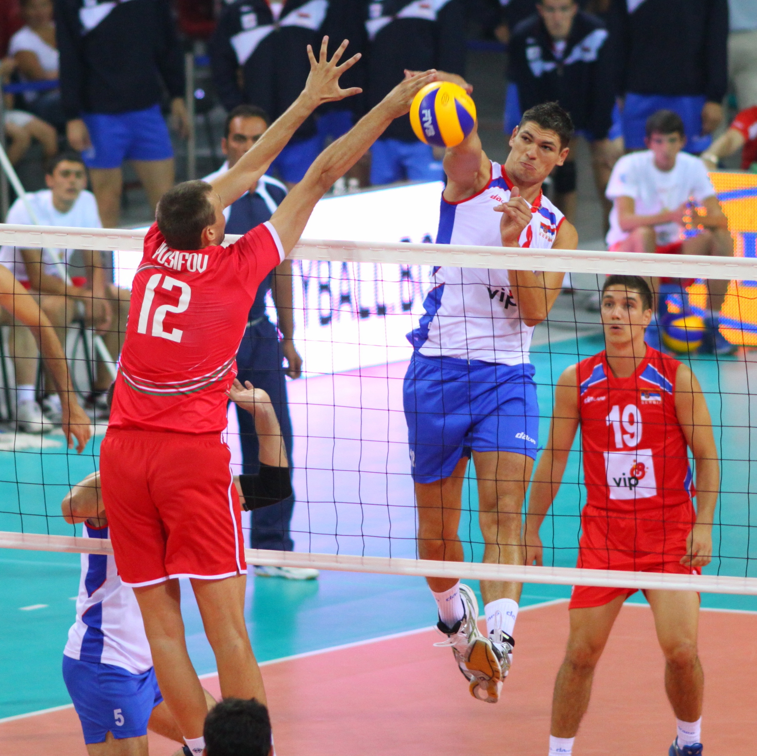 2 guys in an intense volleyball match where one is spiking and one is blocking.