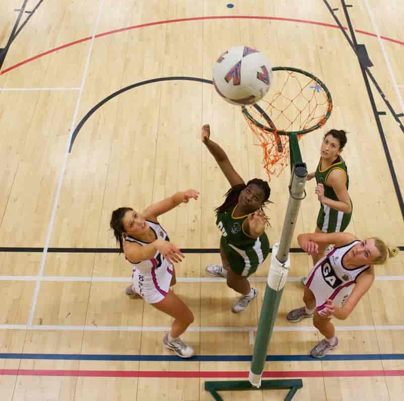 2 teams of women play netball, with one person throwing the netball.